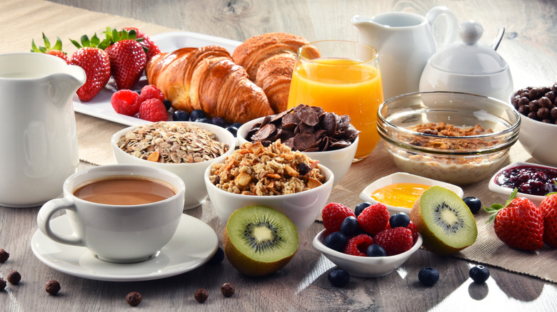 Array of breakfast foods like cereals, pastries, fruits, and coffee on table