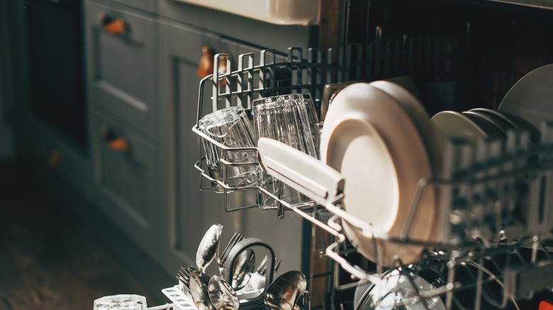 An open dishwasher with racks full of dishes and silverware