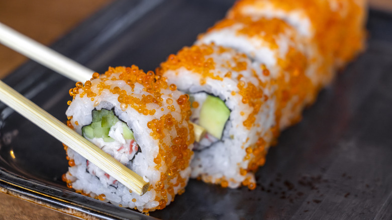 Person grabbing salmon sushi roll with chopsticks