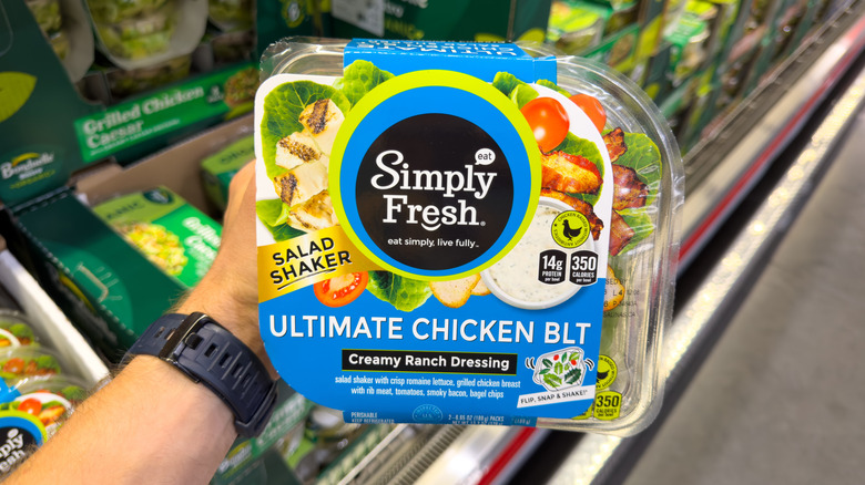 man's hand holding a pack of a Simply Fresh salad shaker kit in Costco aisle
