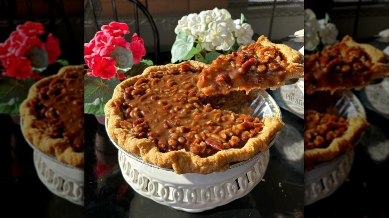 A serving spatula removing a slice of pumpkin praline pie from a stand with flowers in the background