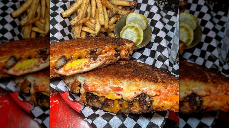 Gwarled cheese sandwich filled with meat on a tray alongside fries and pickles