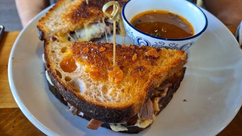Grilled cheese containing veal on a plate alongside a bowl of soup