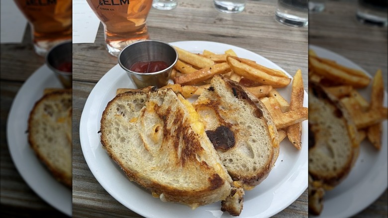 Grilled cheese on a plate with fries and ketchup, with a glass of cider in the background