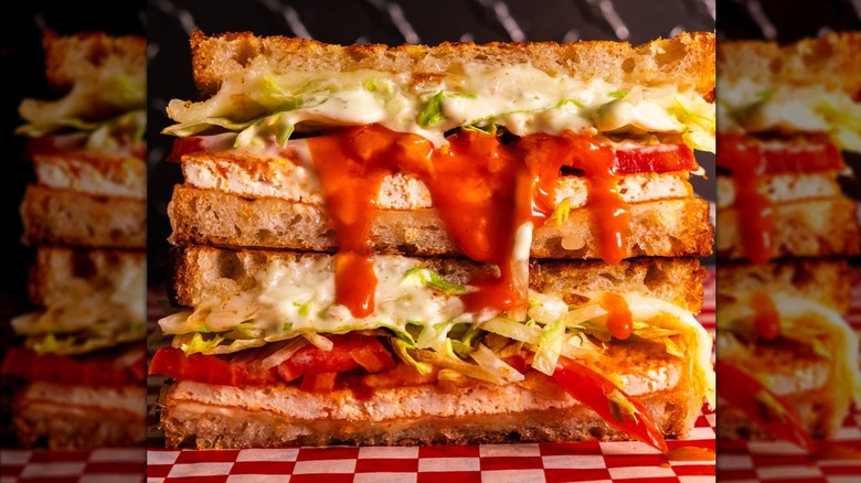 Two pieces of Buffalo tofu melt sandwich stacked atop one another with Buffalo sauce dribbling down the side