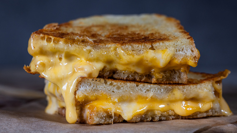 Two halves of a grilled cheese sandwich stacked atop one another with cheese melting down the side