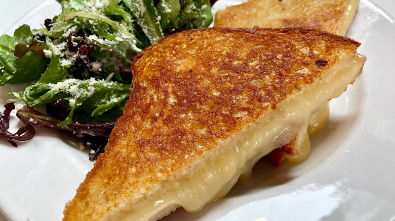 Grilled cheese cut in half, served on plate alongside salad greens