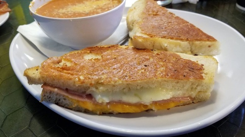 Grilled cheese sliced in half and served on plate with bowl of soup