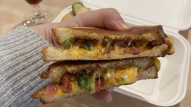 Hand holding Fig Pig grilled cheese in front of takeout box