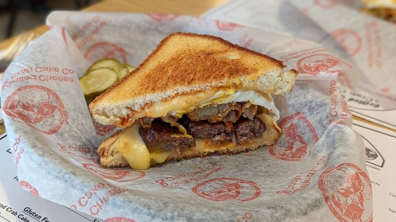 Half a grilled cheese served with pickles on basket lined with paper