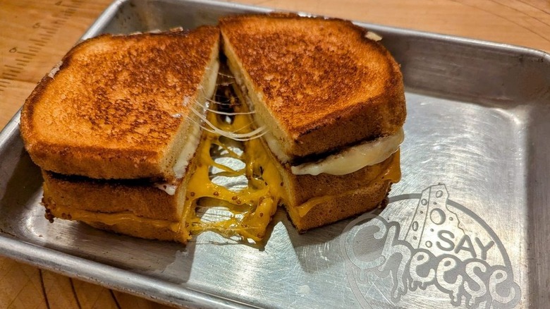 Thick grilled cheese on metallic serving tray, cheese stretching between two halves