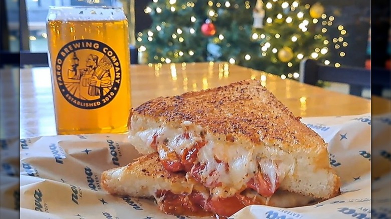 Fancy grilled cheese nestled in Nova Eatery-branded paper with a pint of beer