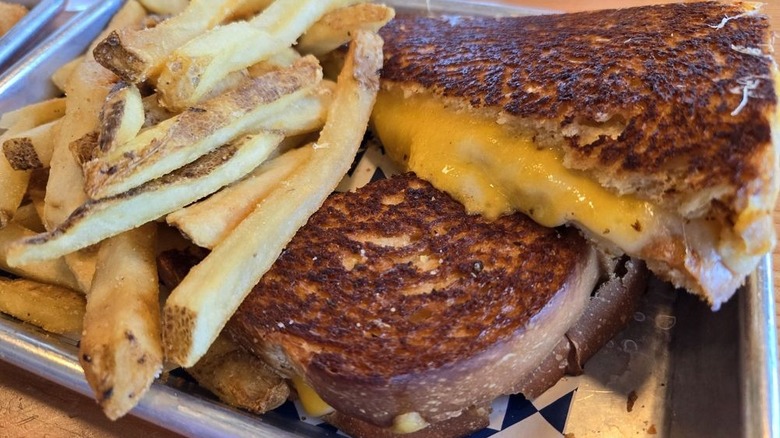 Grilled cheese cut in half along with fries on metallic serving tray
