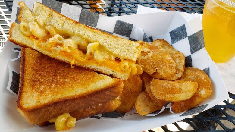 Grilled cheese stuffed with macaroni alongside chips on disposable serving tray