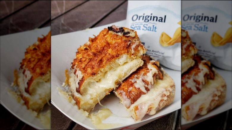 Grilled cheese pretzel sliced in half on serving tray with bag of chips