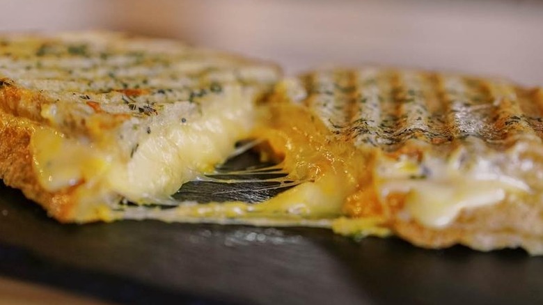Two halves of grilled cheese sandwich on slab, pulled apart to show cheese stretching