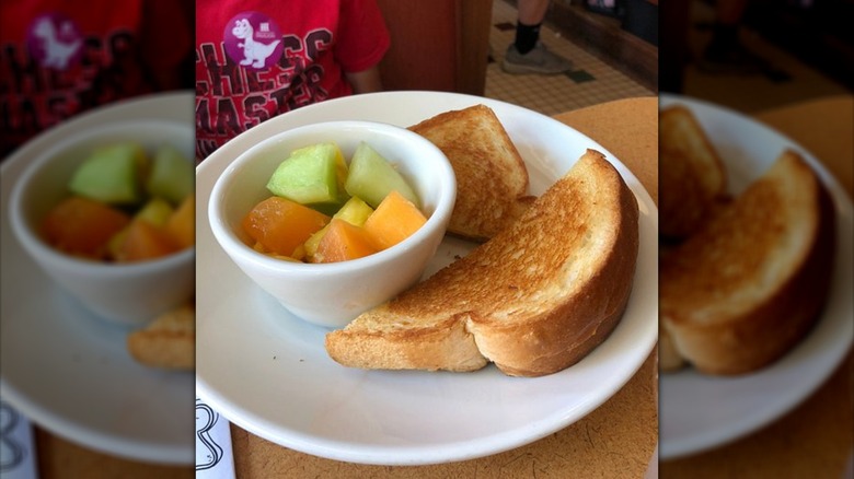 Grilled cheese sliced in half, served on plate with bowl of fruit