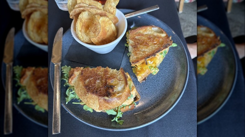 Grilled cheese with arugula spilling out, sliced in half and served on plate with chips