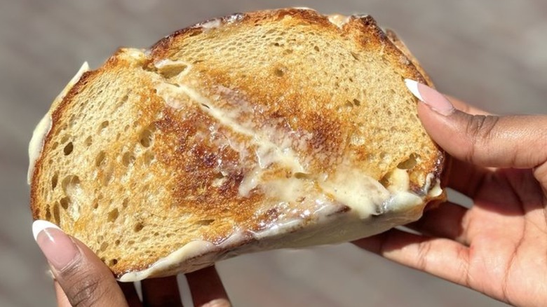 Hands holding grilled cheese sliced diagonally in half