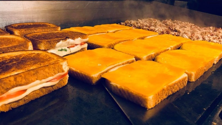 Grilled cheese sandwiches in various states of preparedness on large grill