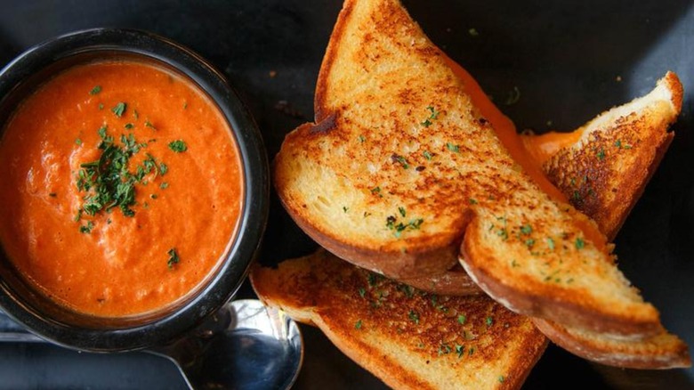 Grilled cheese sliced in half, served alongside spoon and bowl of soup