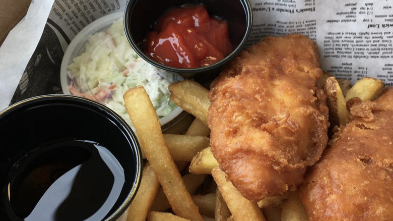 Fried fish and fries with condiments on newspaper