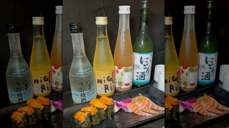 Sushi and nigiri on black plate and four bottles of Japanese alcoholic beverages