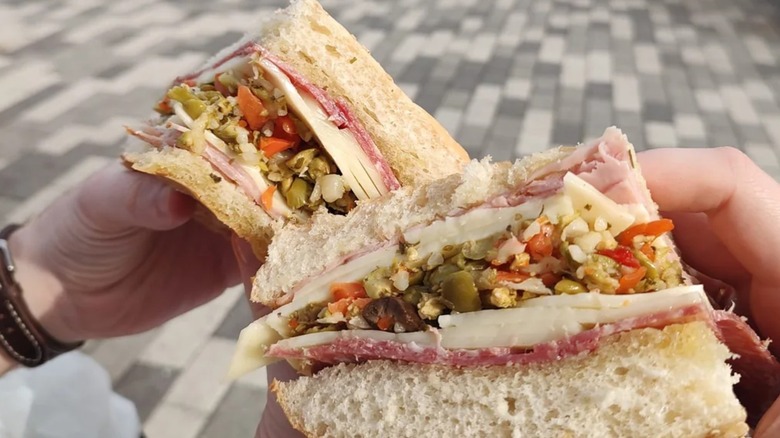 Hands holding halvse of a muffuletta sandwich outside