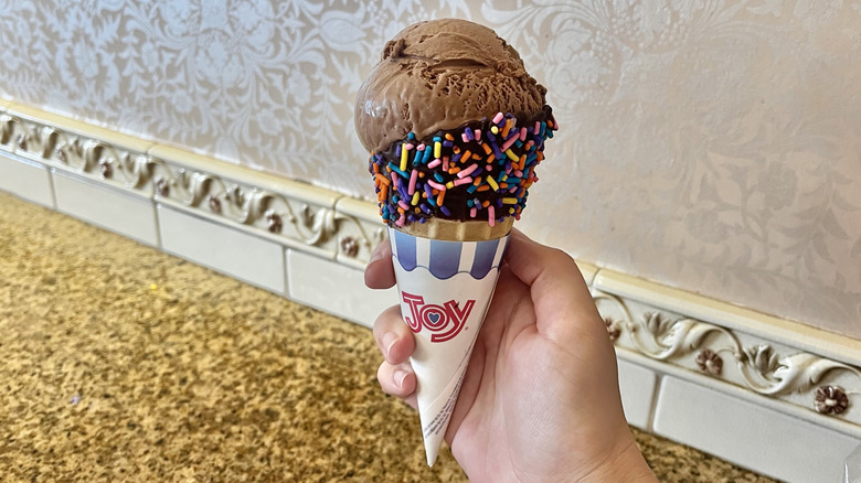 Hand holding a dipped ice cream cone with chocolate and sprinkles