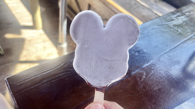 Hand holding a very icy Mickey ice cream bar in front of a wooden table