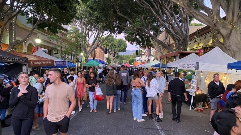 Shoppers strolling between tents on street underneath trees strung with lights