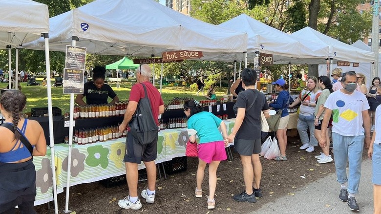 Shoppers examining hot sauce selection at farmers market in park