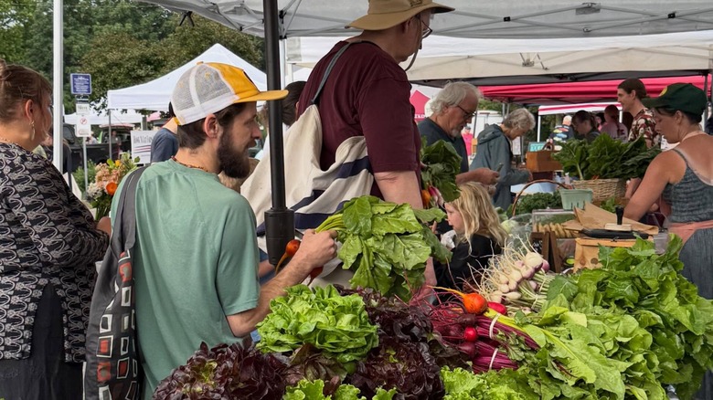 Shoppers standing in line to buy leafy greens under tent