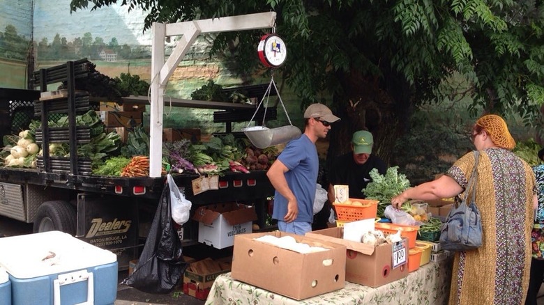Shopper buying produce from farmer in front of large hanging scale and truck