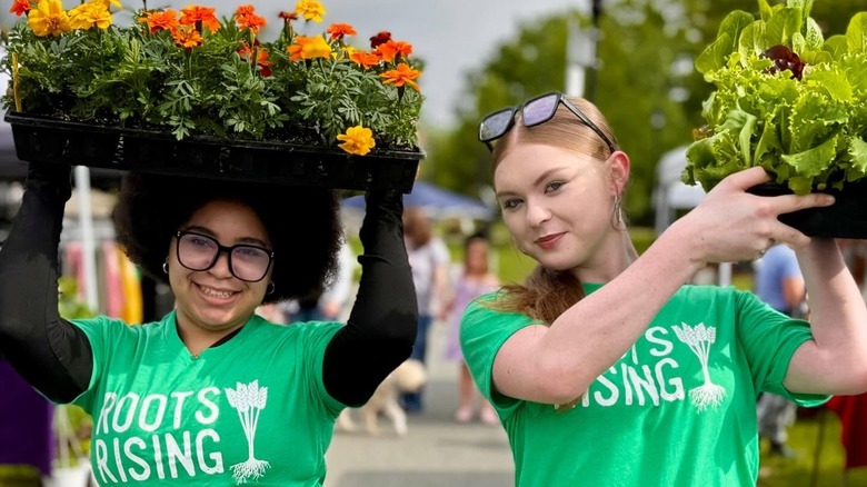 Two teenager girls, one holding up lettuce and the other holding up flowers
