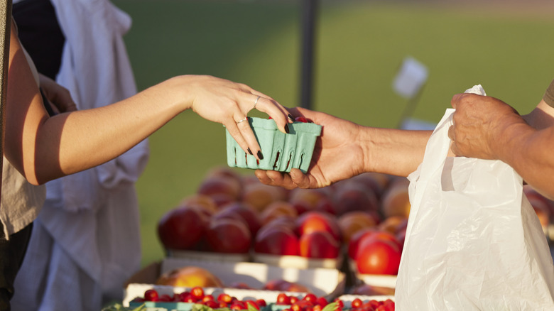 Customer handing carton of cherry tomatoes to vendor to put in bag