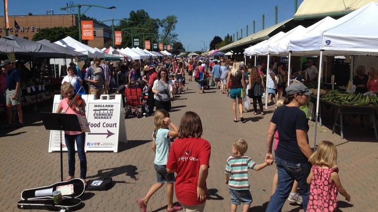 Families walking around farmers market while young girl plays violin