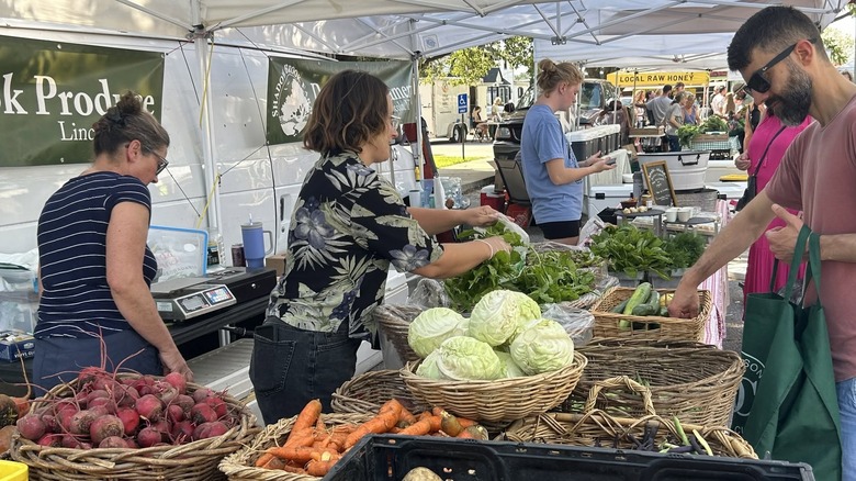 Shoppers browsing selection of root vegetables, cabbages, zucchinis, and leafy greens