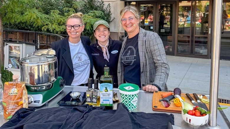 Three women behind table, prepared for cooking demonstration