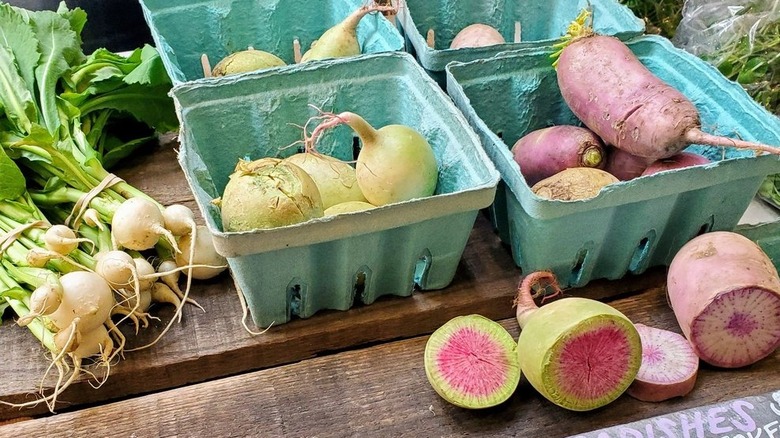 Radishes and turnips, some in cartons, for sale on wooden table