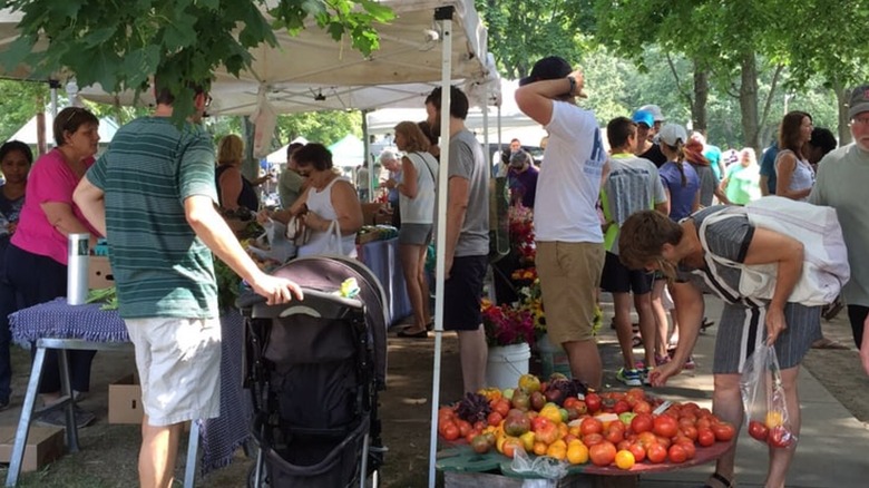 Woman leaning down to pick tomatoes amidst crowded market