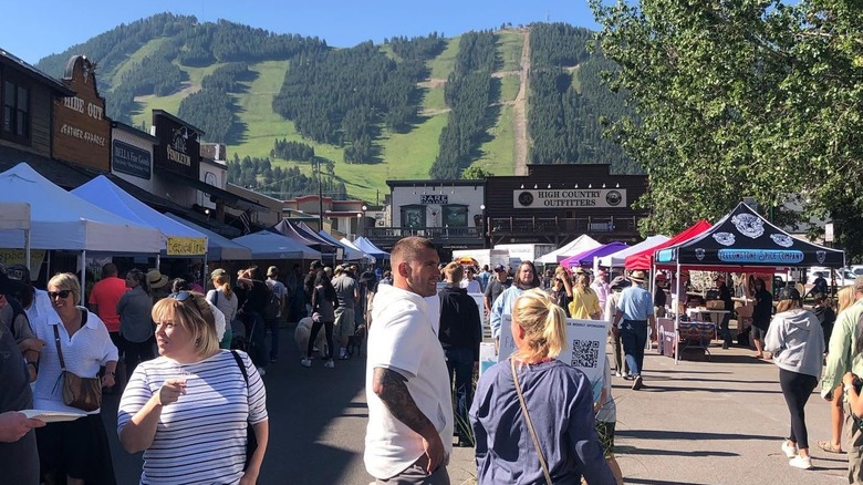 Shoppers perusing farmers market with ski slope in background