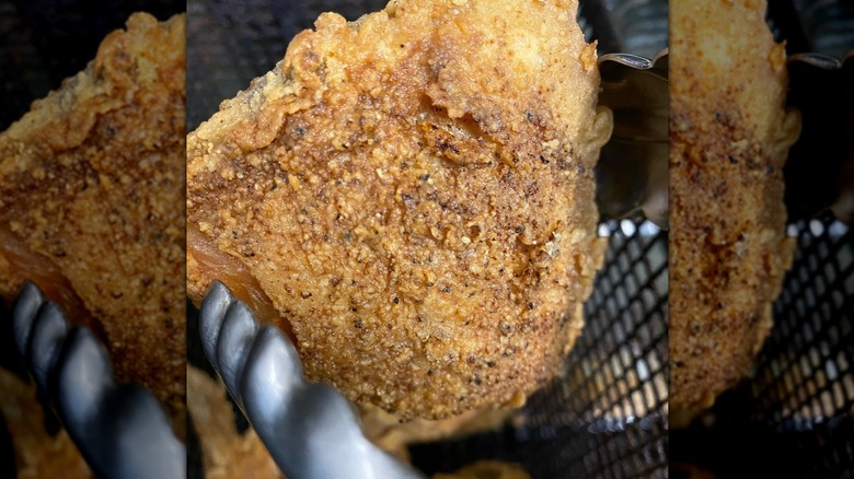 Close-up of piece of seasoned fried chicken held by tongs