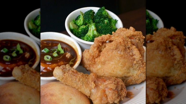White plate with fried chicken next to bowl of gravy and bowl of broccoli