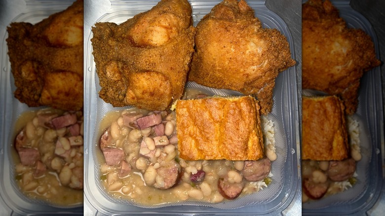 Top-down shot of takeout container with fried chicken, cornbread, beans and sausage