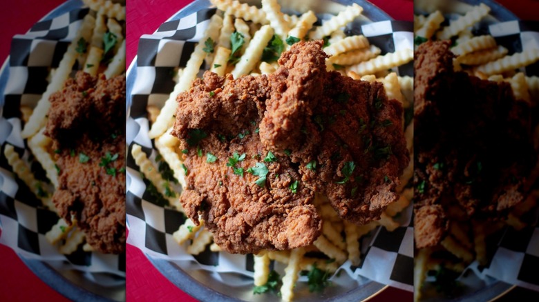 Top-down shot of chicken topped with parsley on a basket of crinkle cut fries