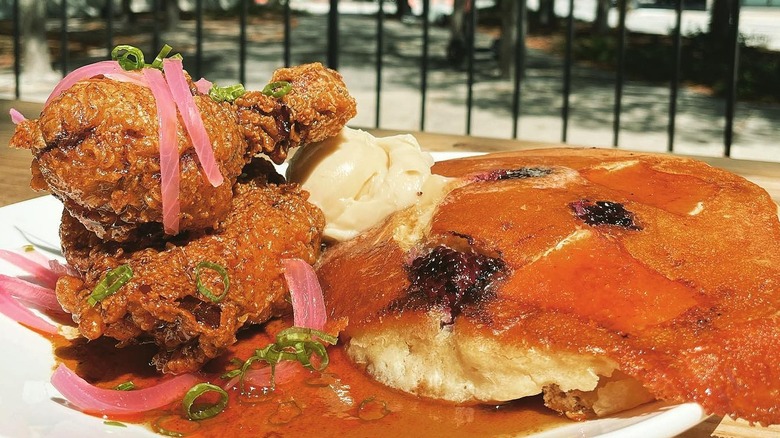 Fried chicken next to pancakes with pickled red onions on white plate