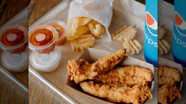 Tray of food with sauce cups, waffle fries, chicken tenders, Pepsi