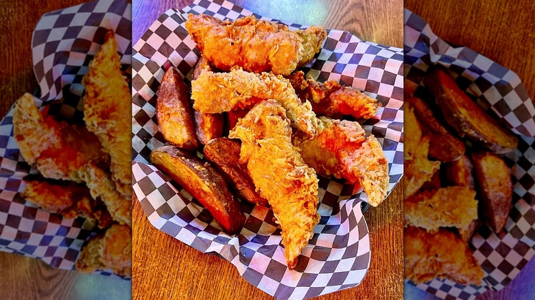 Basket of chicken tenders and wedge fries on wooden table