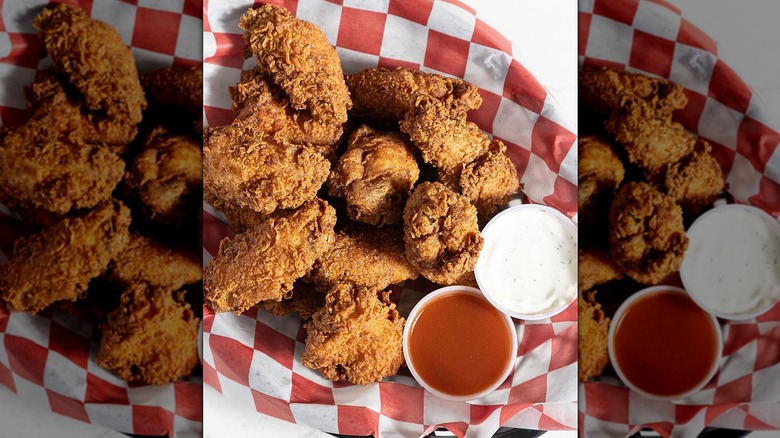 Top-down view basket of fried chicken and two cups of sauce on red checkered paper